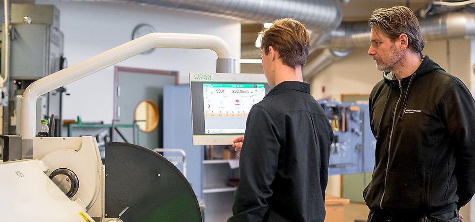 Elev står vid en industriteknisk maskin med en skärm. En lärare står bredvid.