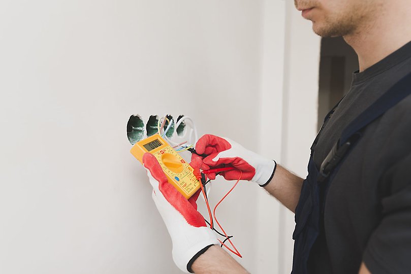 Manlig student som håller i en elmätare vid ett vägguttag.